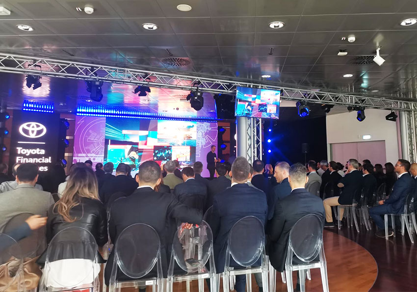 Platea all'evento Toyota Financial Service che guarda il relatore sul palco personalizzato con luci e schermi